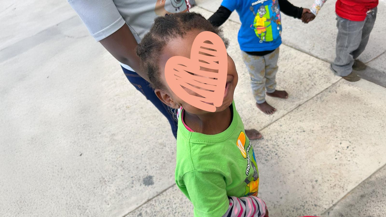 a little girl, waiting for a family, looks up at the camera while she holds hands with others in a circle