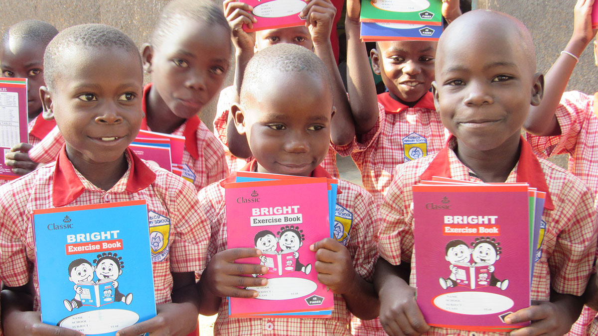 Kids in Uganda hold up workbooks they received thanks to Holt sponsors
