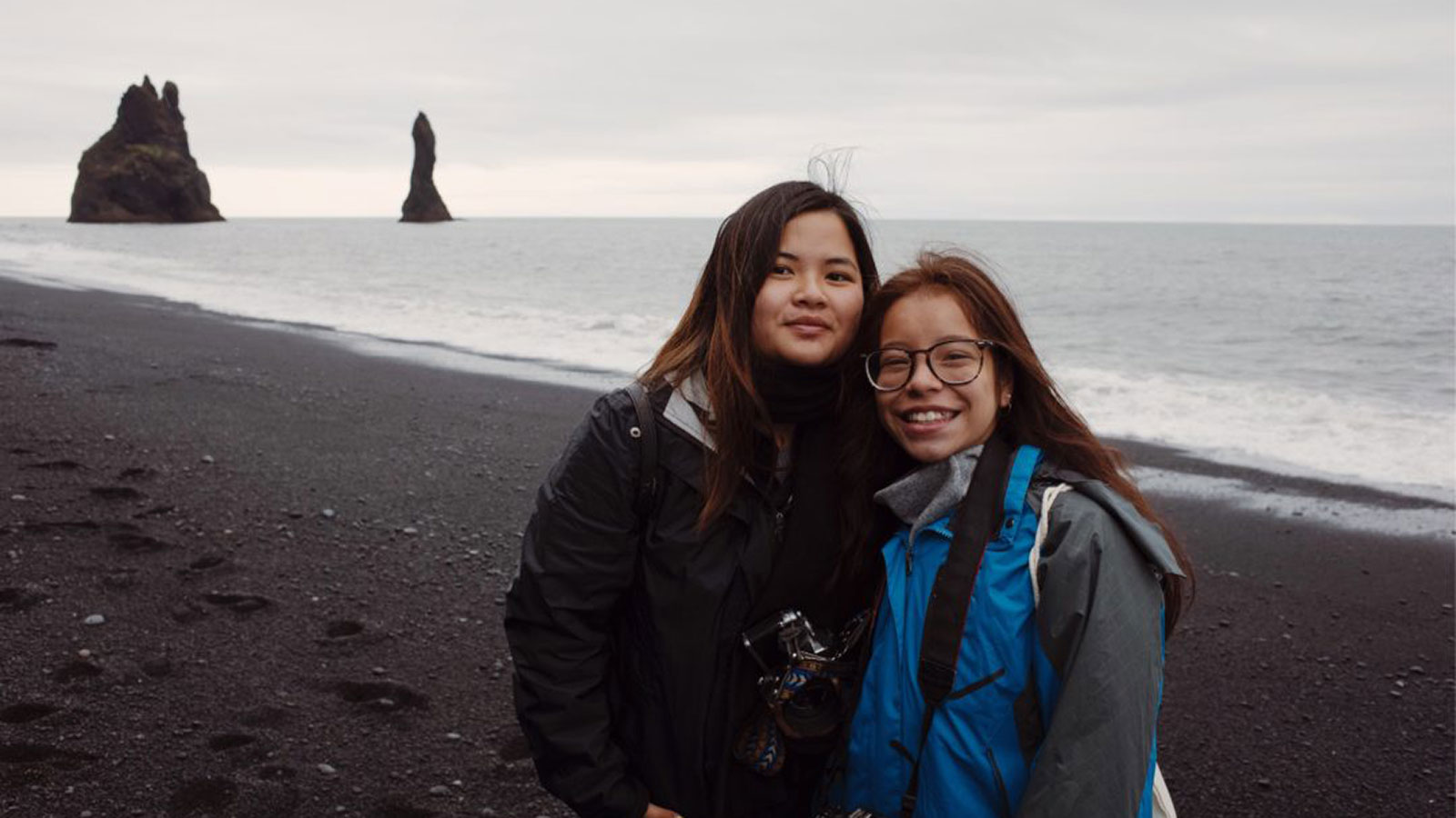 two girls with their arms around each other at a cold and windy beach