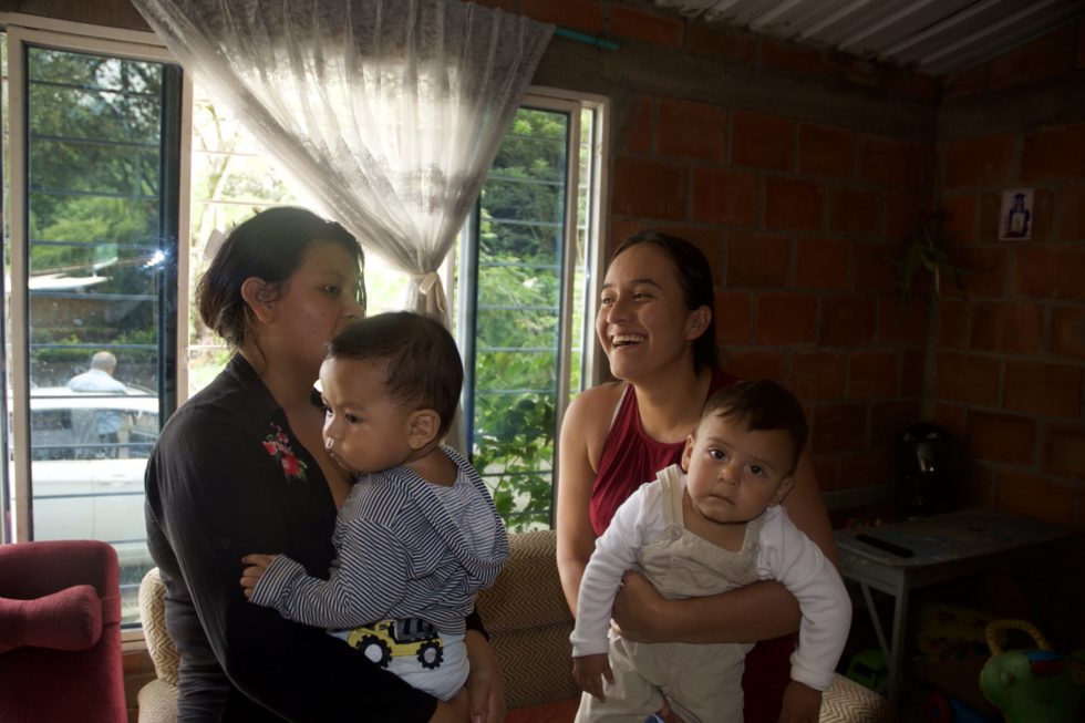 Diana and Johanna laugh together in Johanna's living room, their sons in their arms. 