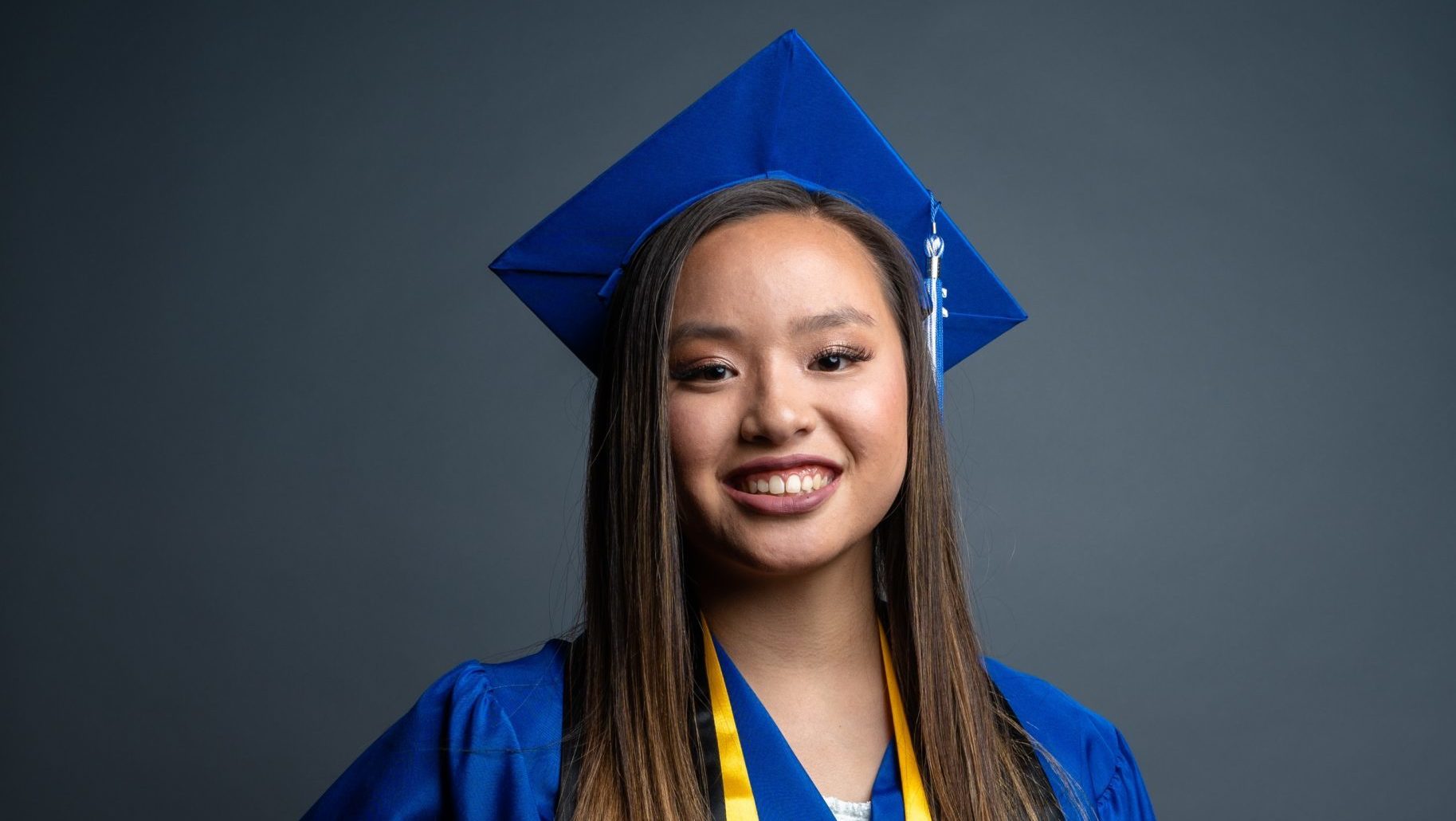 smiling girl standing with one hand on hips wearing blue graduation cap and gown