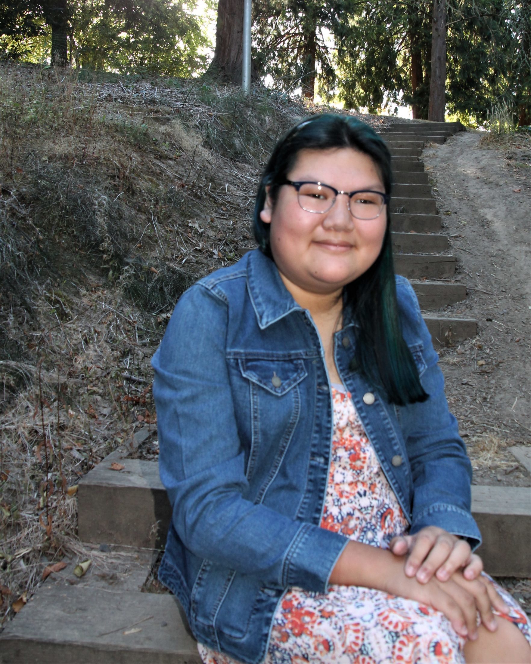 smiling girl sitting on stairs wearing printed dress and denim jacket