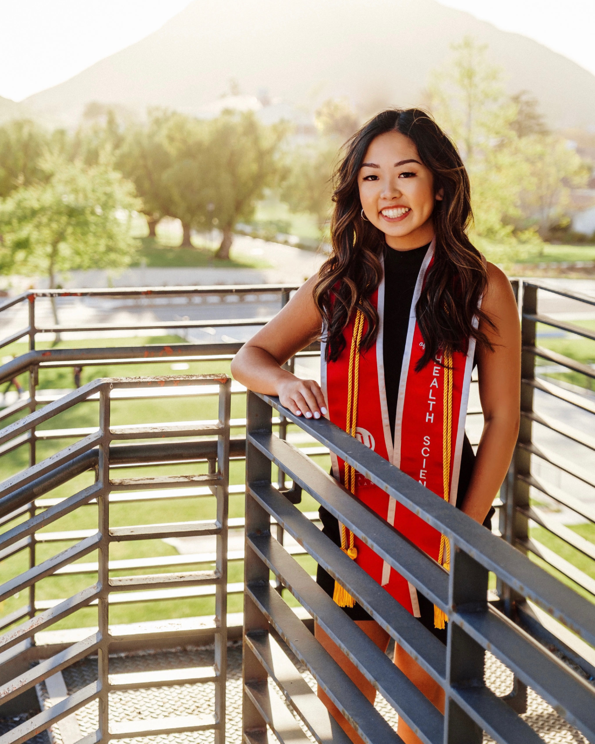 smiling girl standing on sunlit staircase wearing black dress and red sash