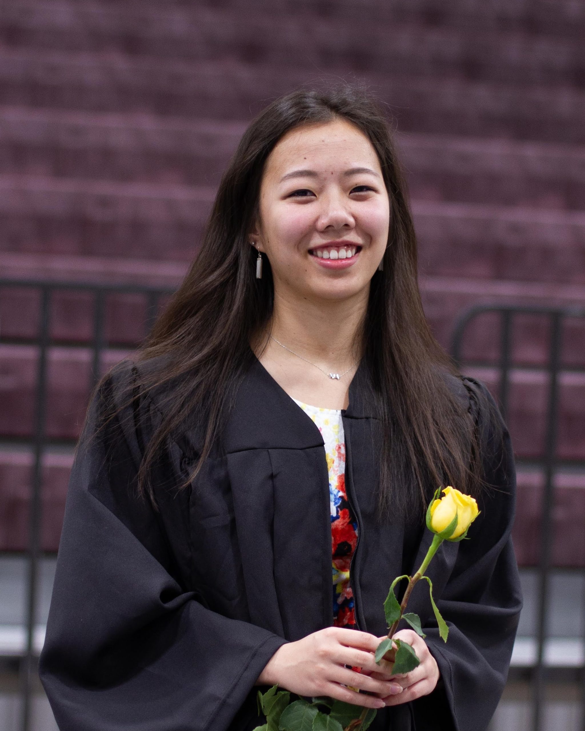 smiling girl wearing black graduation gown and holding yellow rose