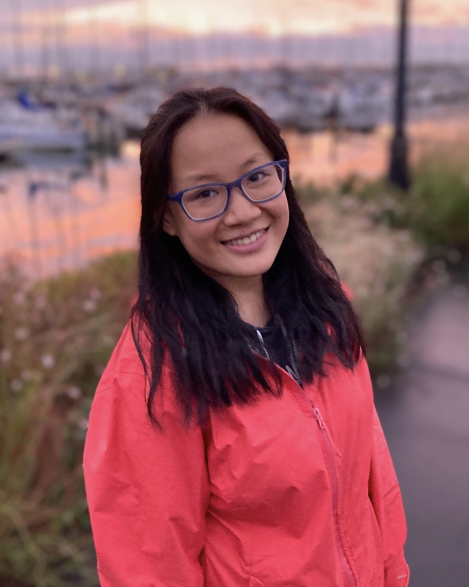 smiling girl in pink raincoat standing near a dock during sunset