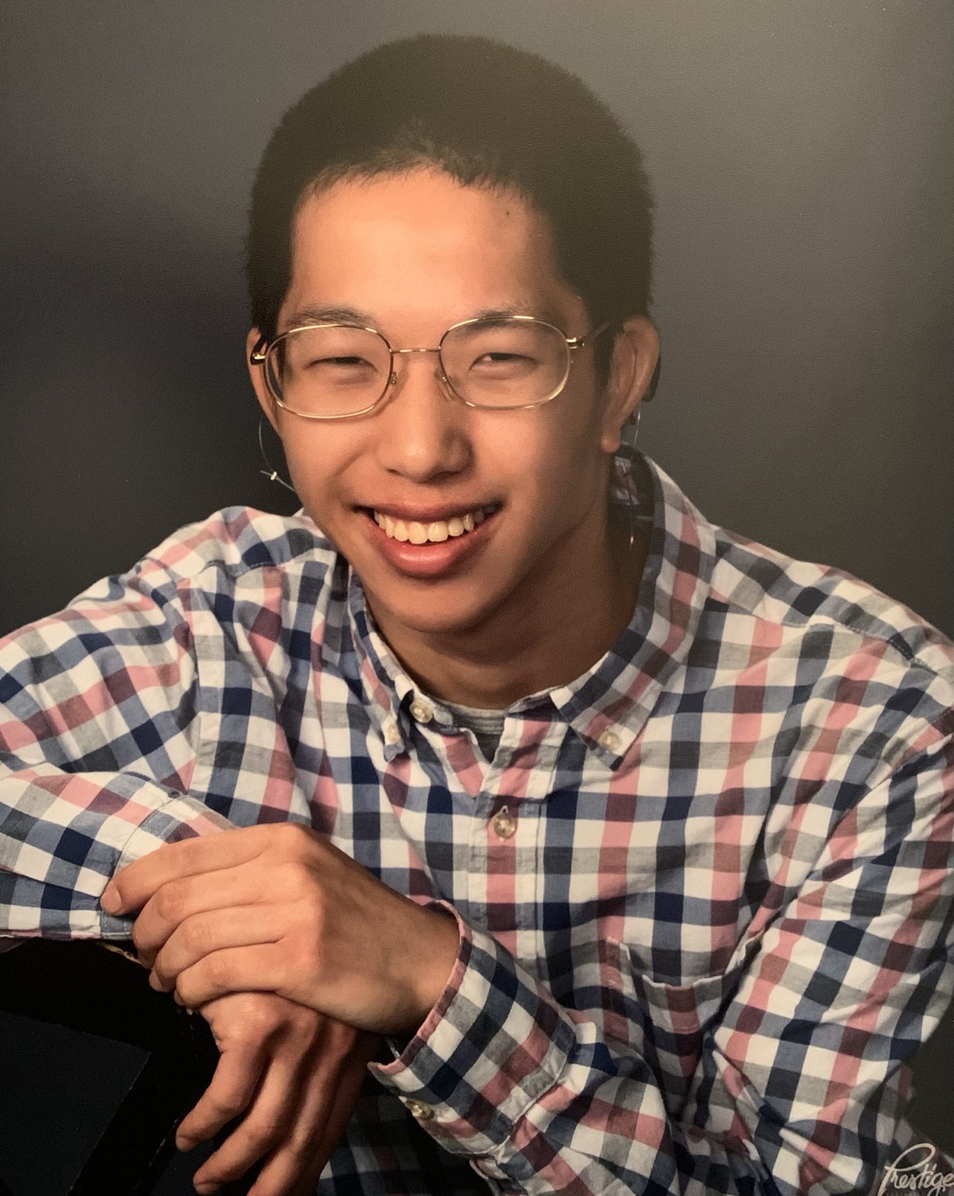 smiling man wearing plaid shirt and glasses with hands on his knee