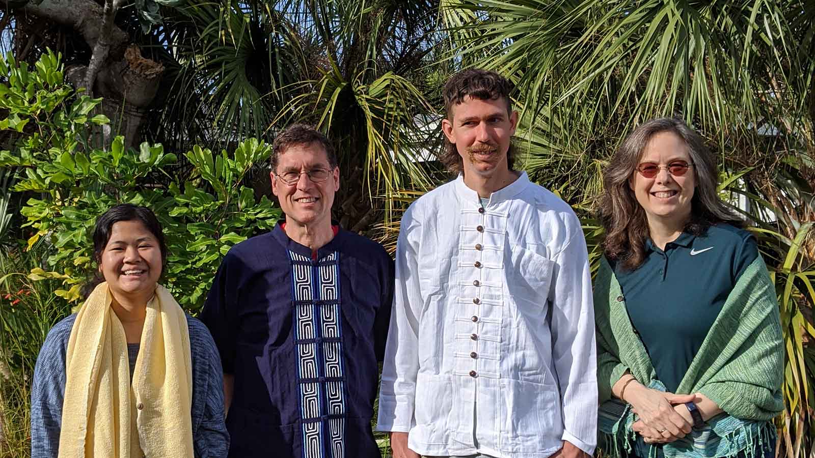 four people standing in front of palm trees smiling