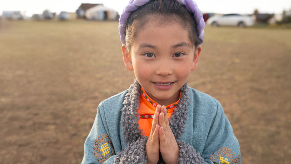 Little girl holding hands like a prayer, in a field in mongolia, smiling