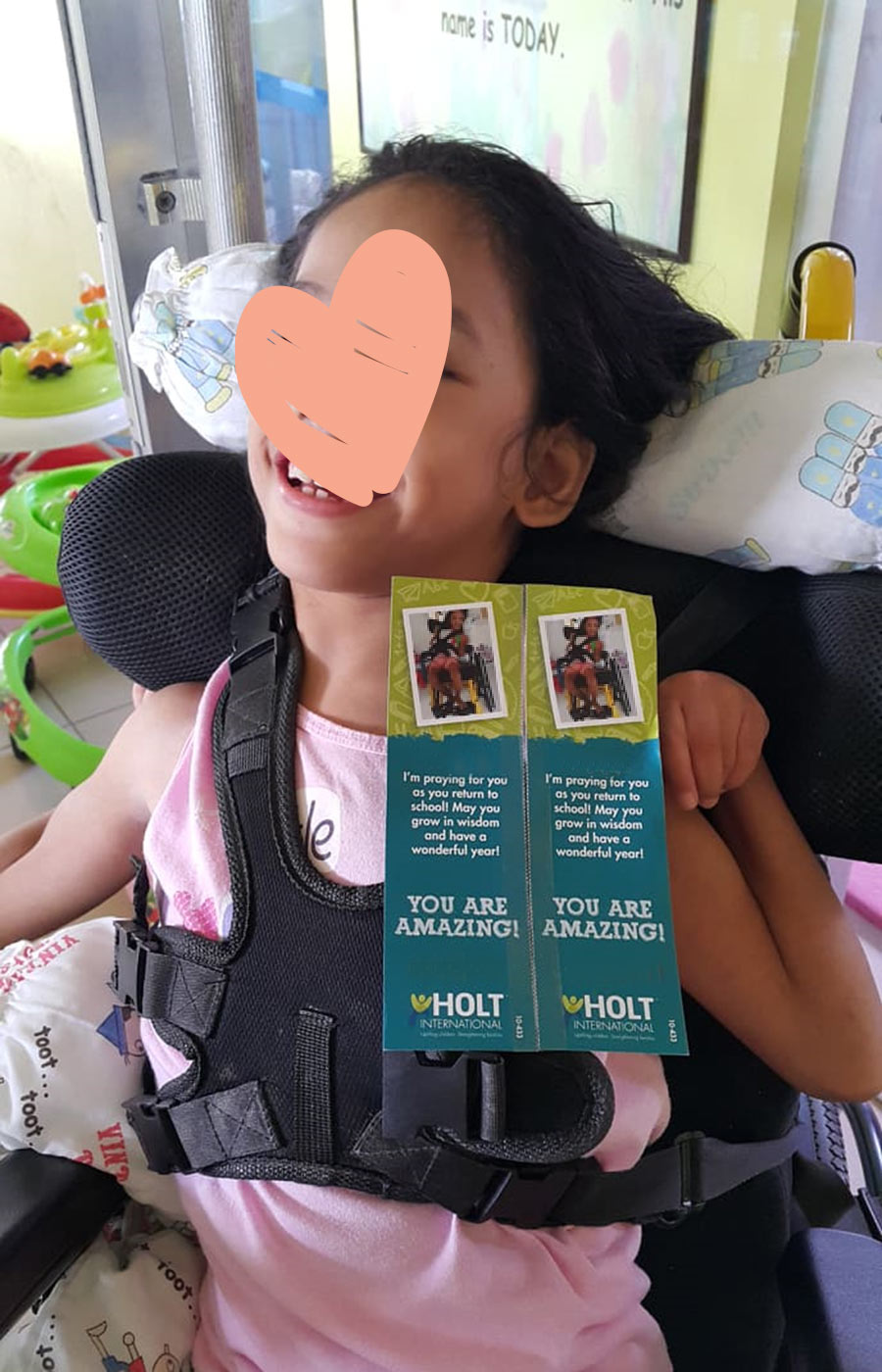 smiling child with face hidden by heart graphic holding Holt sponsorship booklet