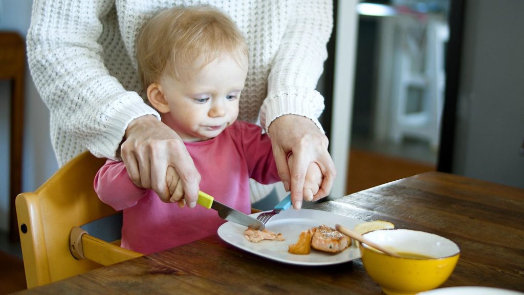 mother helping her baby cut a piece of salmon
