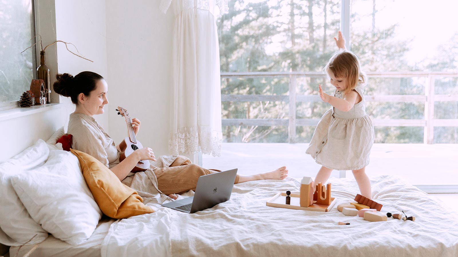 mother playing guitar while daughter dances on the bed