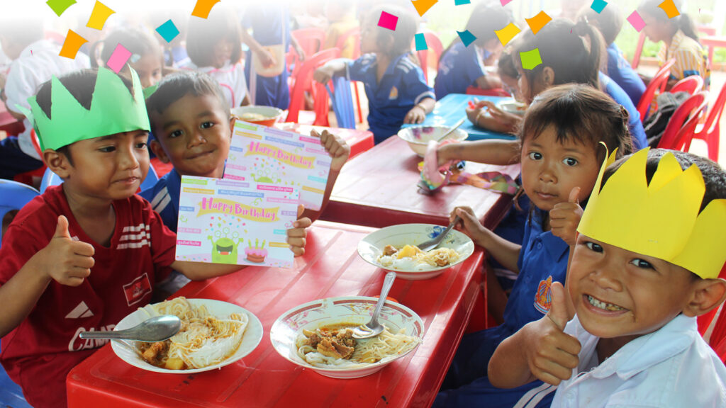 Kids holding birthday cards, eating a meal and smiling at camera