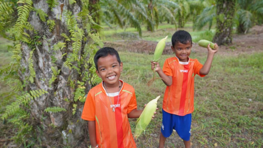 Sponsored twin brothers holding corn stalks on their farm in Thailand