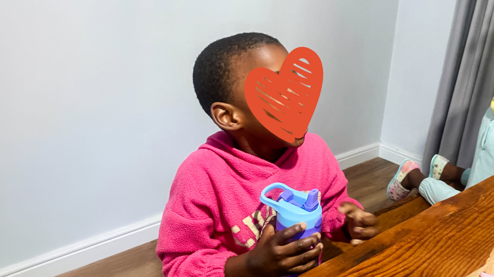 a little girl in a pink shirt and a heart over her face sits at a table with a blue water bottle