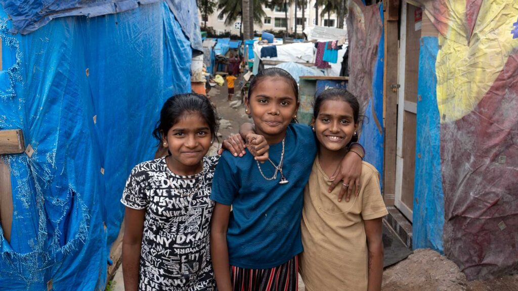 Three young girls standing in a slum in India