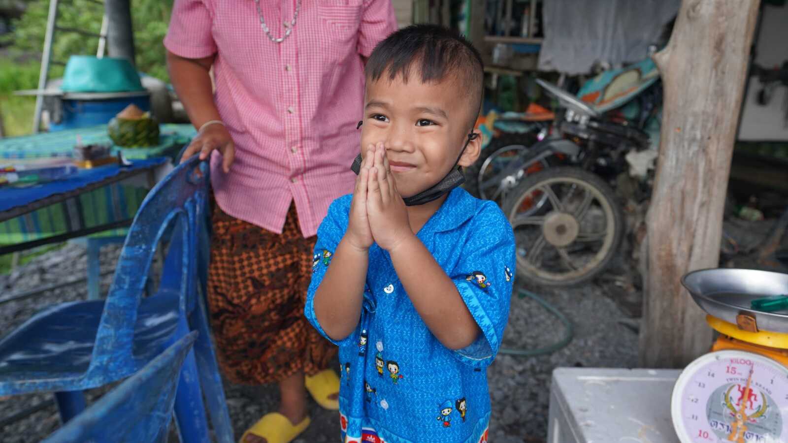 A boy in Holt sponsorship holds his hands in a wai to say hello