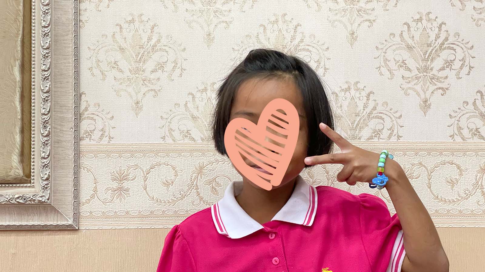 Girl in pink shirt holds up a peace sign