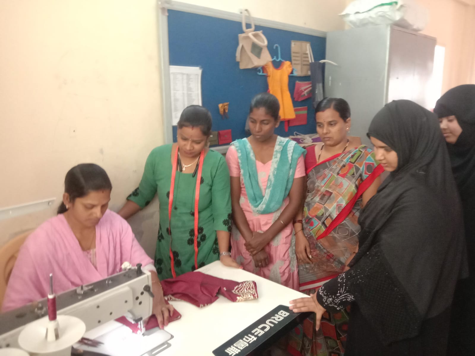 A group of women gathers around a sewing machine, India
