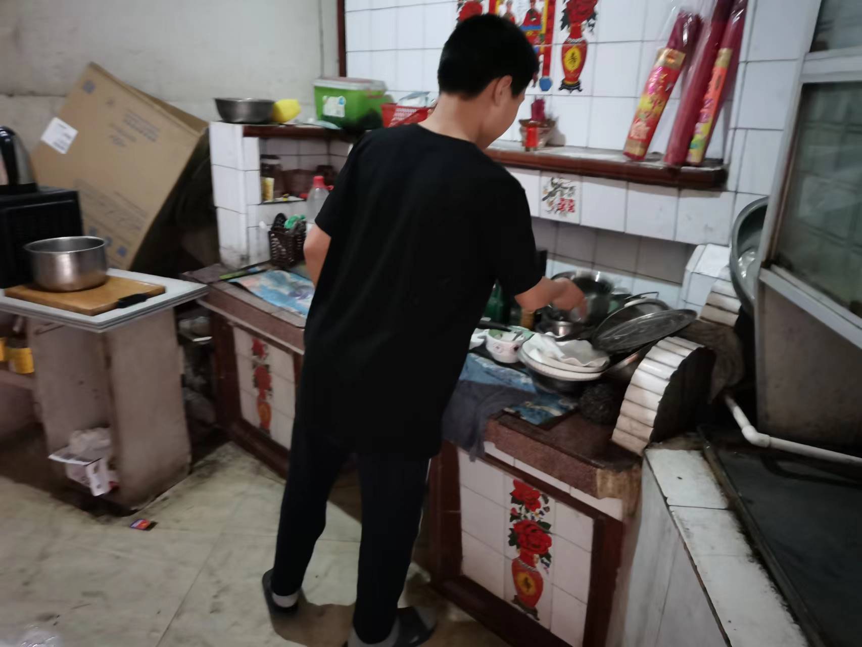 Boy with his back to camera stands at sink doing dishes