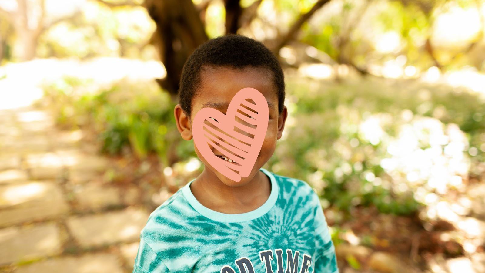 Little boy in blue tie-dye shirt smiles beneath a tree
