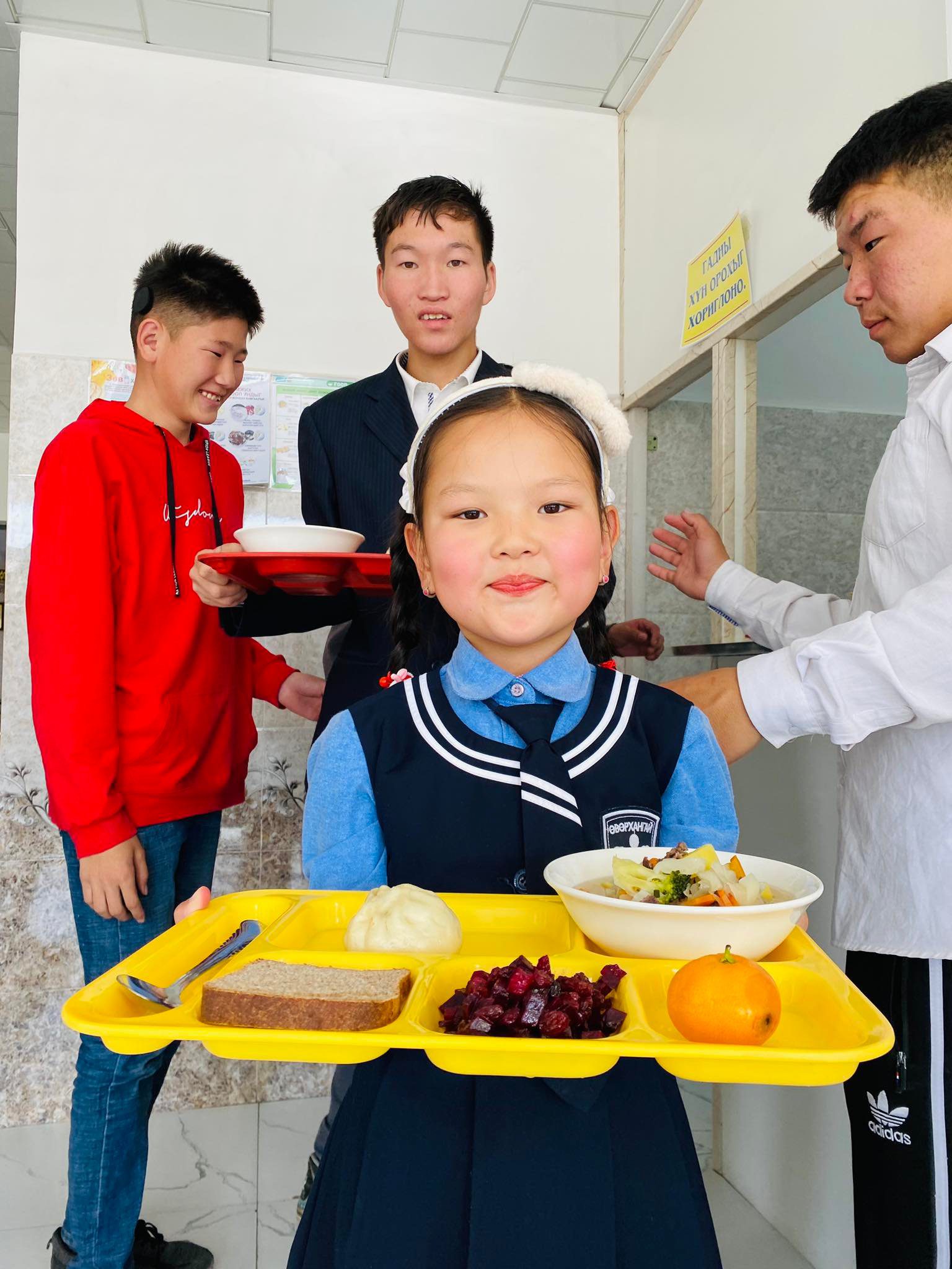 Little girl in school uniform smiles whil holding lunch tray