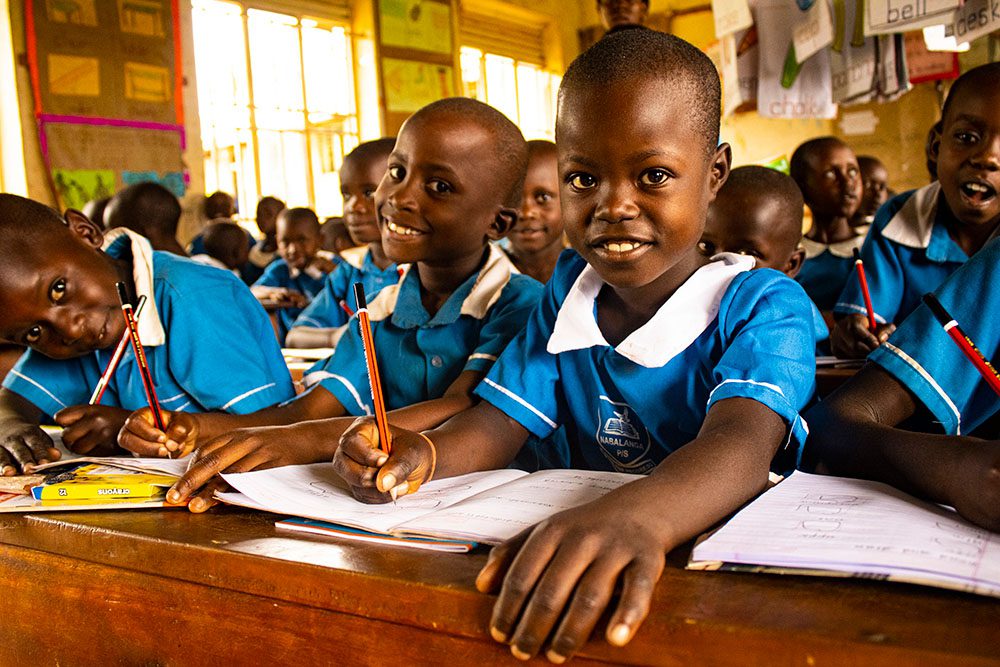 Little girl in school uniform smiles at camera in classroom with book in front of her