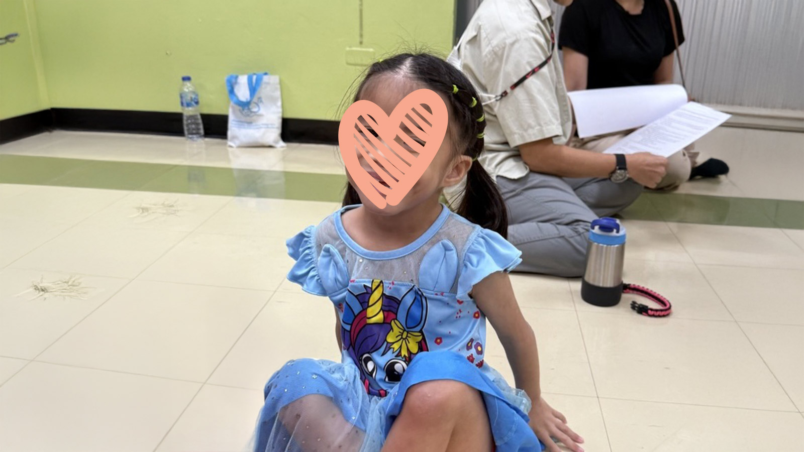a little girl in a blue dress sits on the ground with a heart over her face