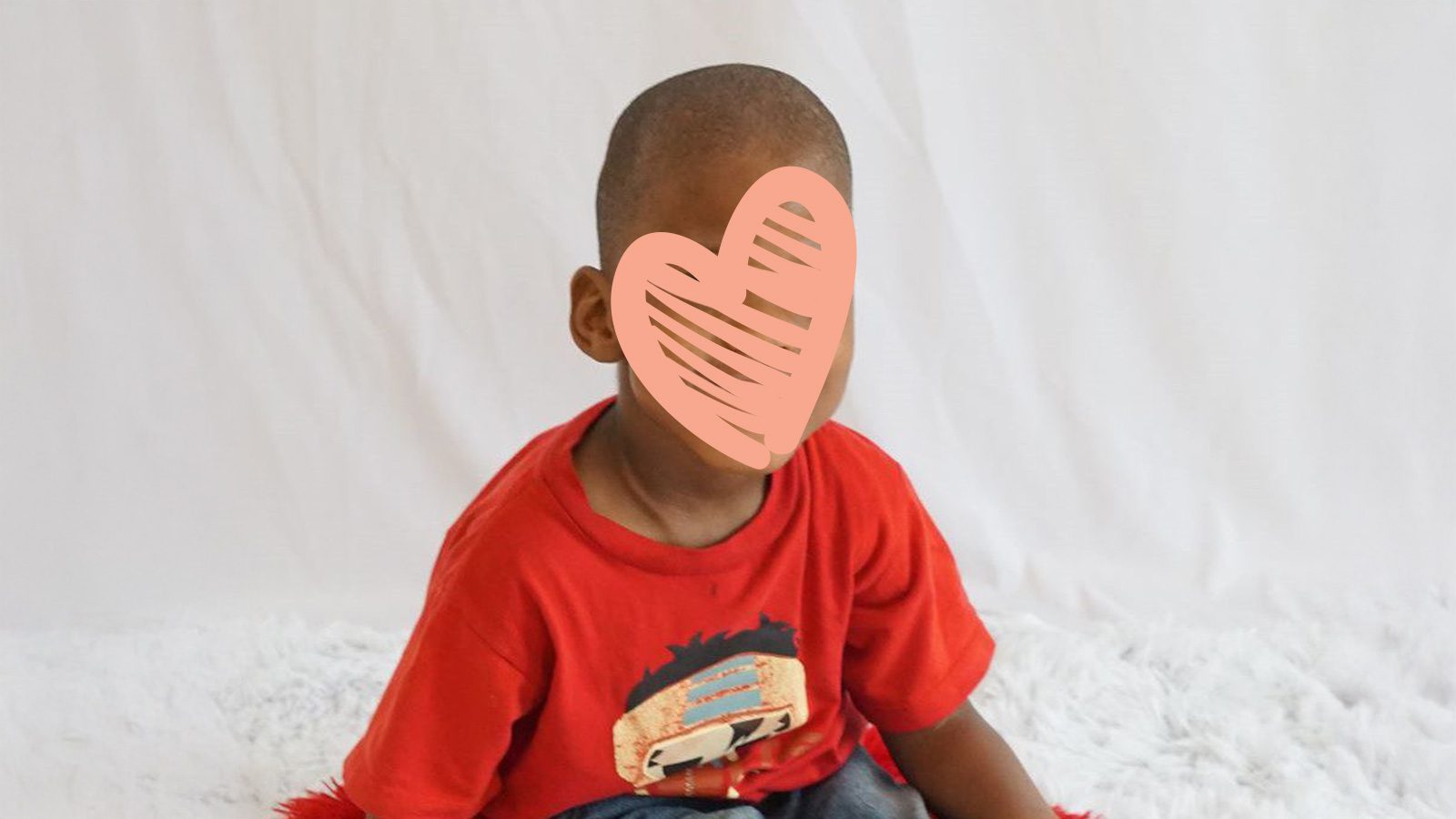 a waiting child sits in a red shirt with a heart over his face