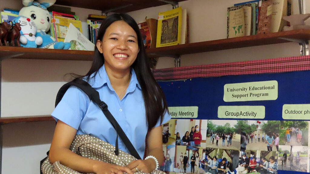 A university student in Cambodia smiles and shows her social work presentation