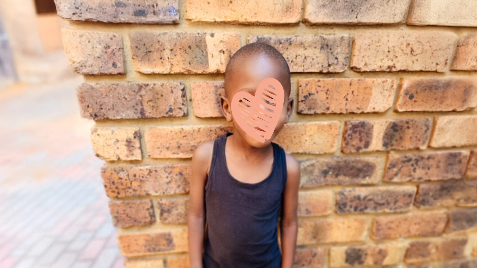 Waiting child Isaac stands against a brick wall