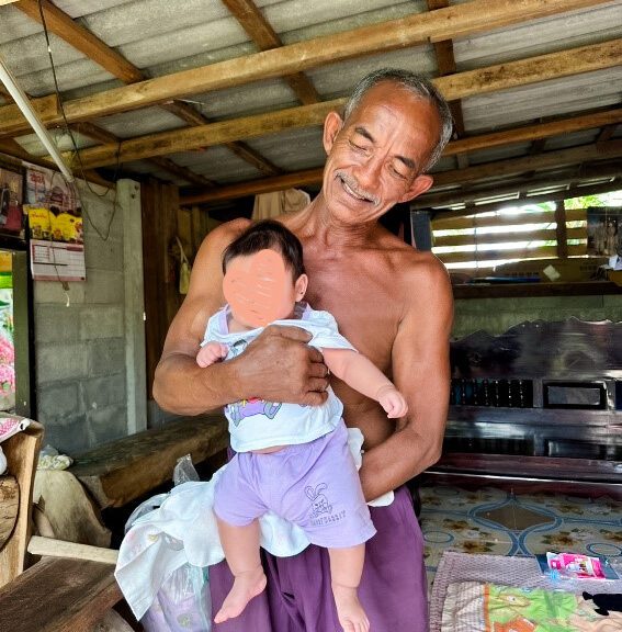 A grandfather holds his infant granddaughter in Thailand.