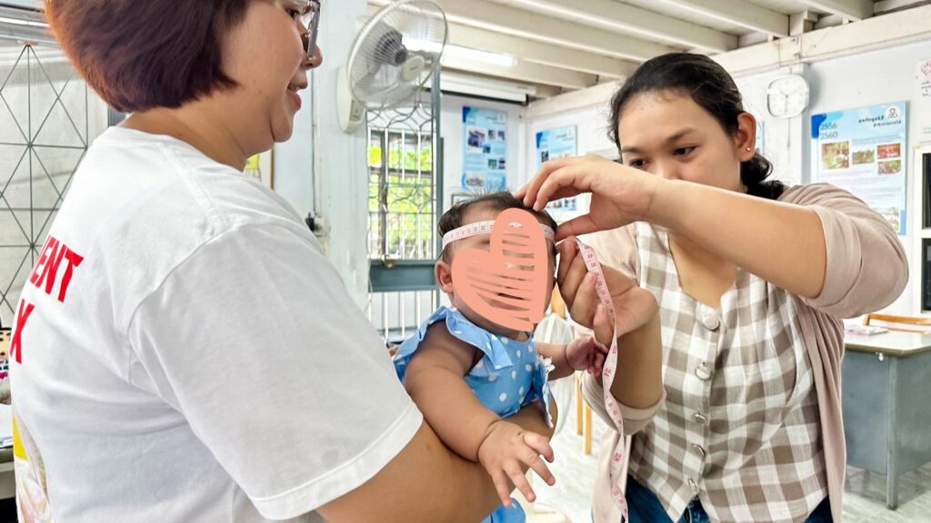 An infant's head is measured by a social worker in Thailand.