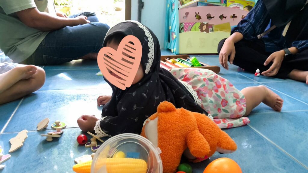 An infant with a heart over her face lays on the floor with toys.