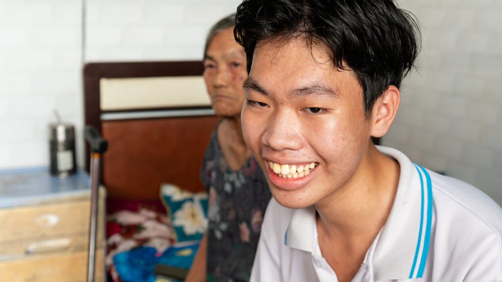 close up of grandson and grandmother sit on the edge of the grandma's bed that is located in the living room