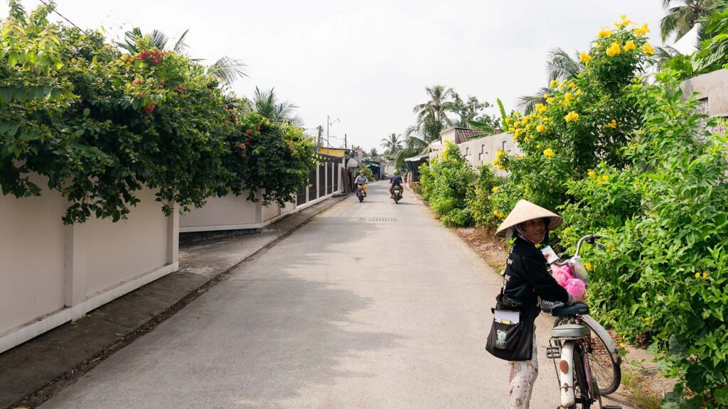 view of the road with motorcyclists in the distance, and a woman selling lottery tickets in the foreground