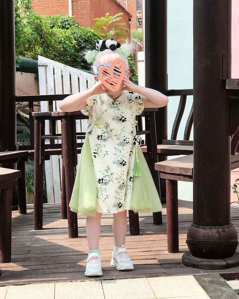 a little girl wearing a panda headband and dress stands with a heart over her face in china