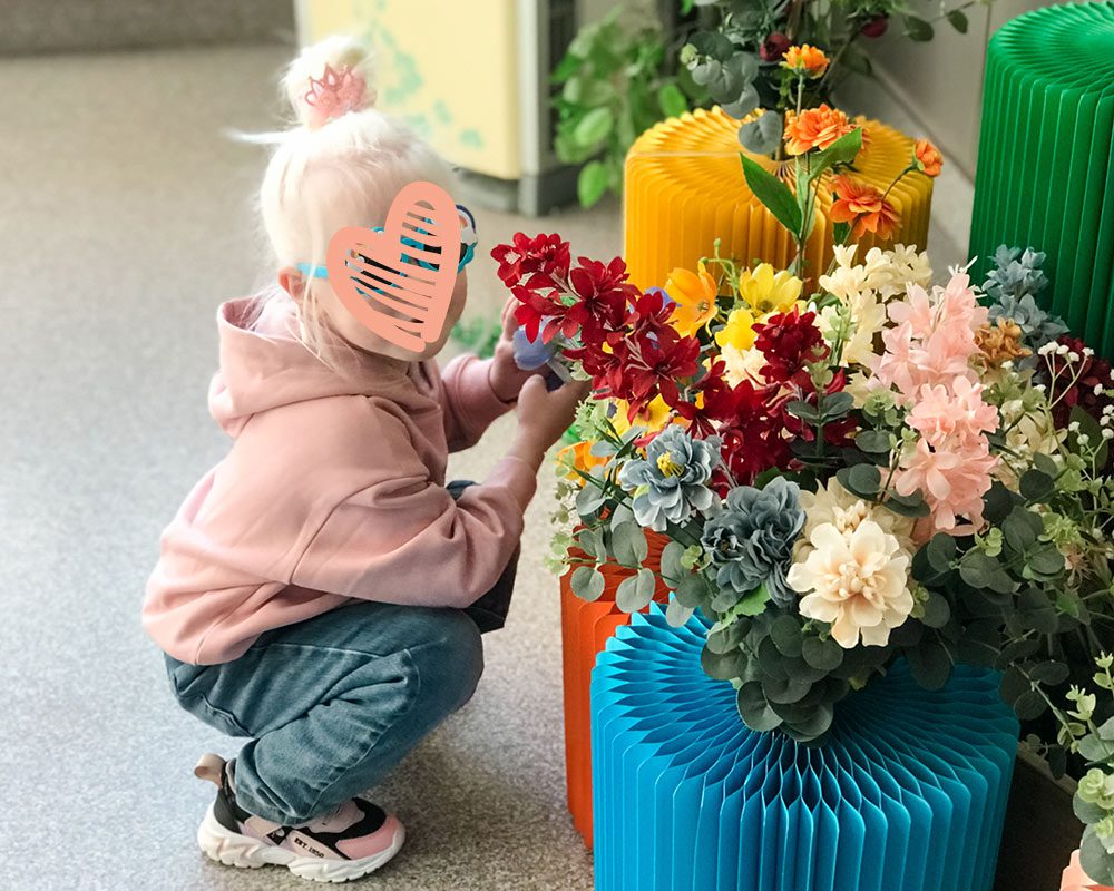 a child with a heart over her face crouches next to a flowerpot in china