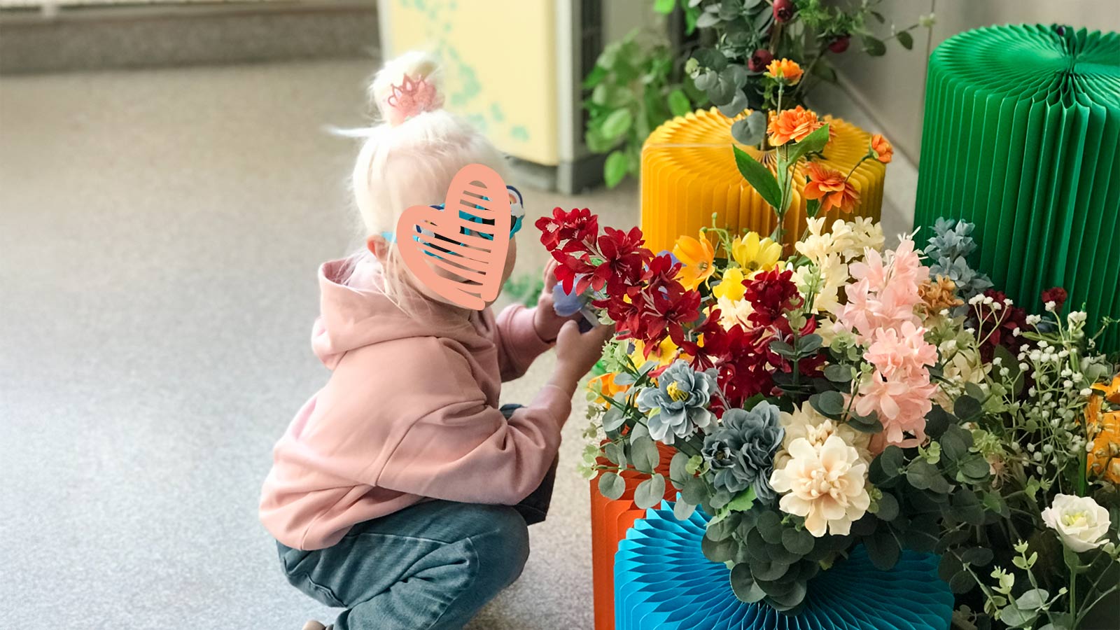 a child with a heart over her face crouches next to a flowerpot in china