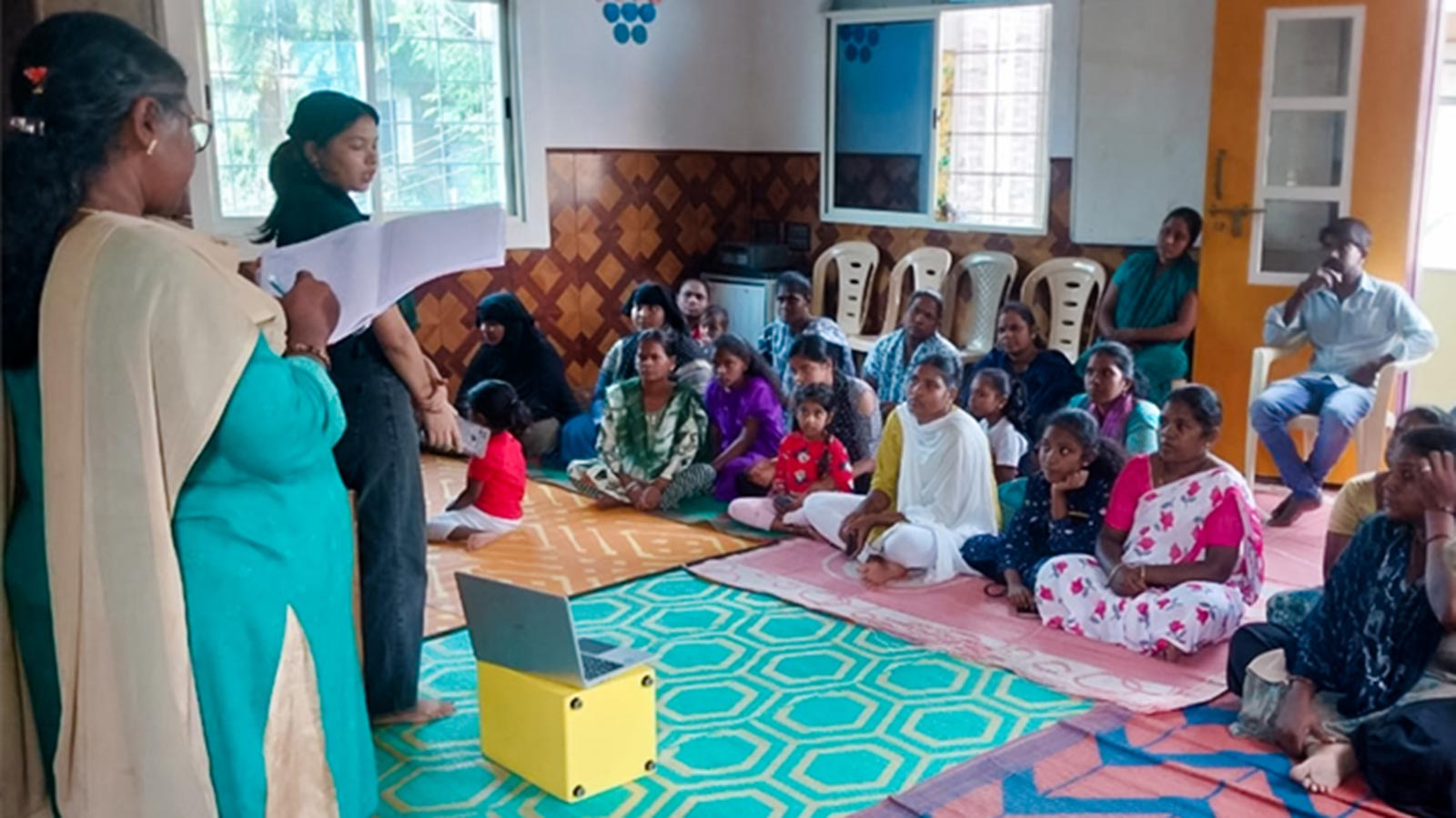 families sit and listen to a parenting education class in India