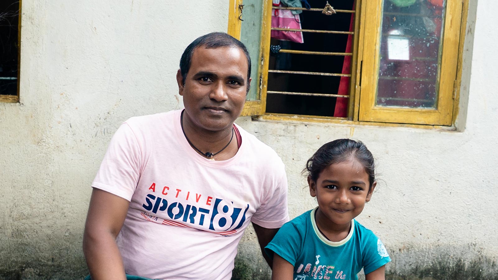 A father and son sit on an outside bench and share their story in India