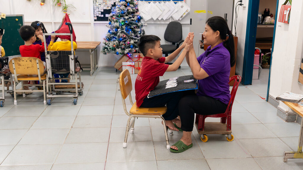 A teacher sits in a classroom interacting with a child
