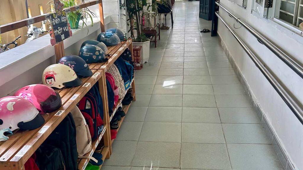 A hallways with tiled floor, and a bookcase of helmets and jackets