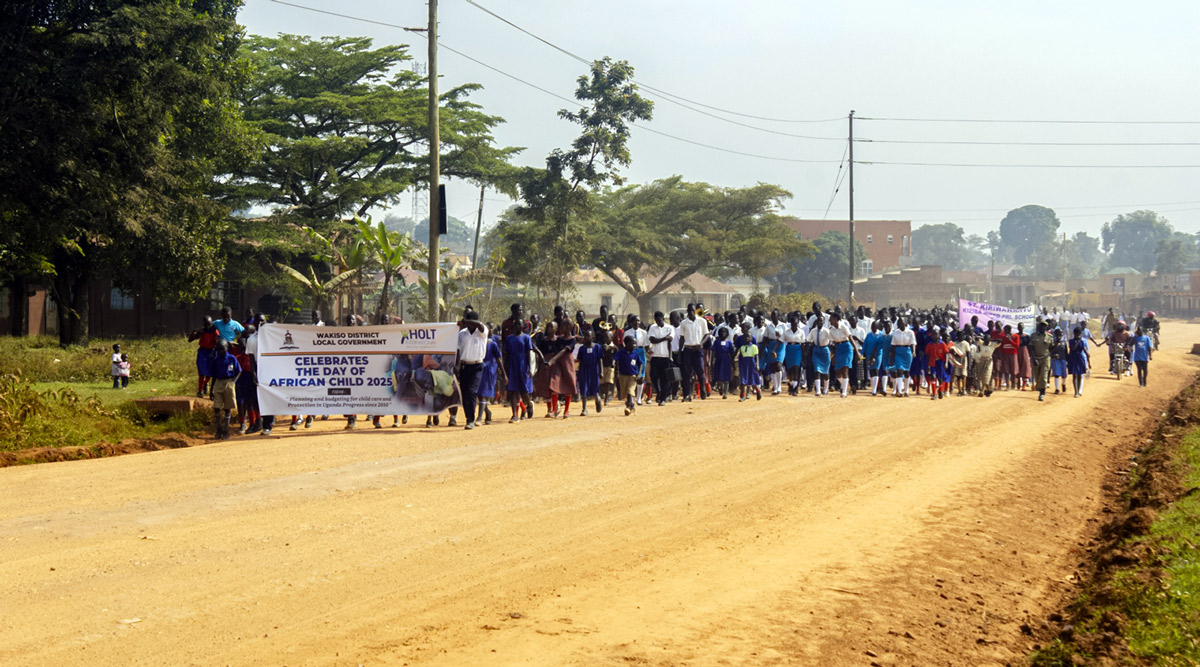 Students and parents walk down a dirt road and celebrate the 2025 Day of the African Child in Uganda
