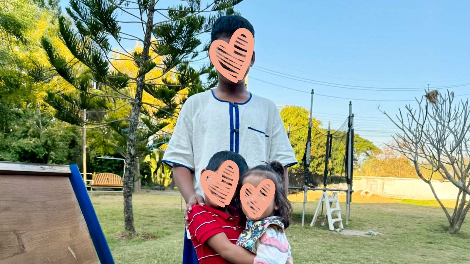 three siblings embrace outdoors, waiting for a family to adopt them.