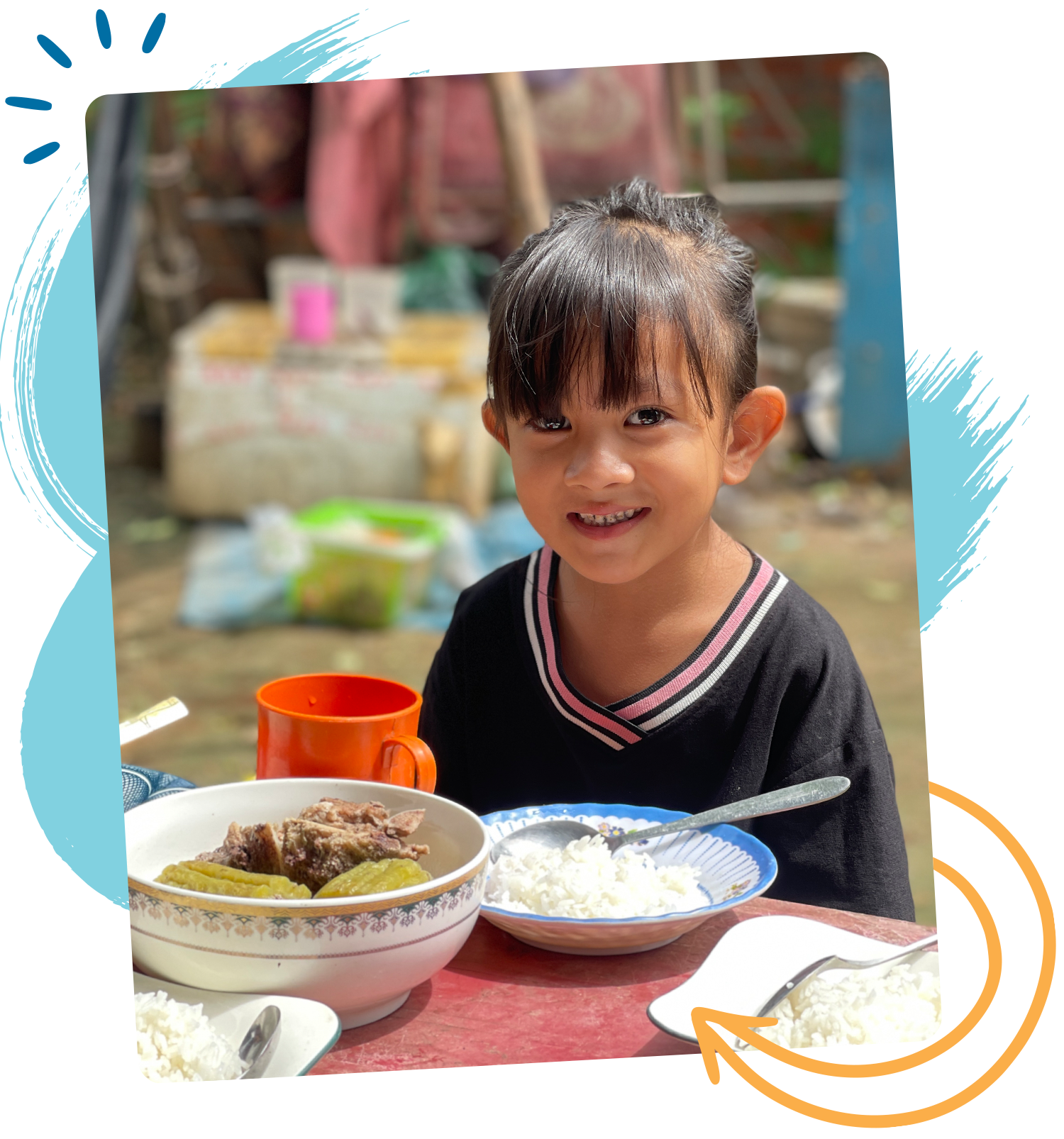 Photo of a little girl smiling with two bowls of food and an orange cup in front of her. 