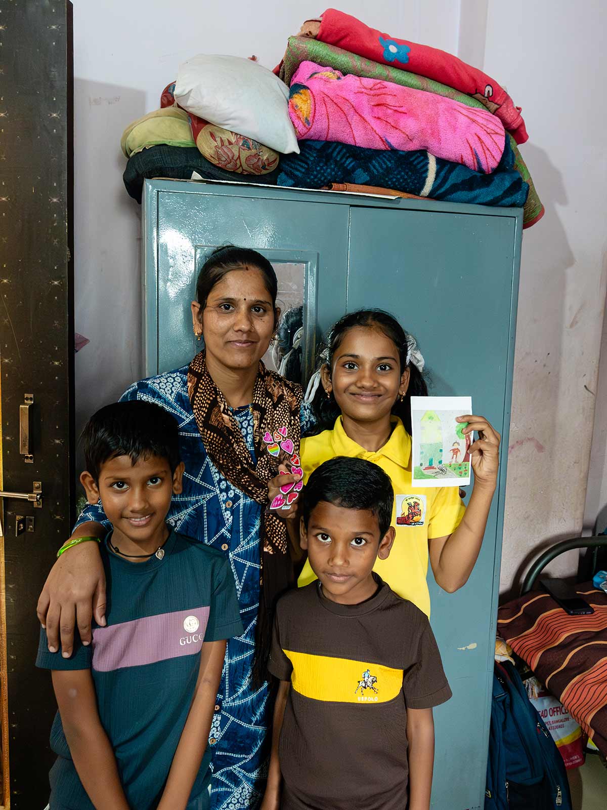 Standing in her home, a sponsored girl smiles with her family and holds up a drawing of her dream home.