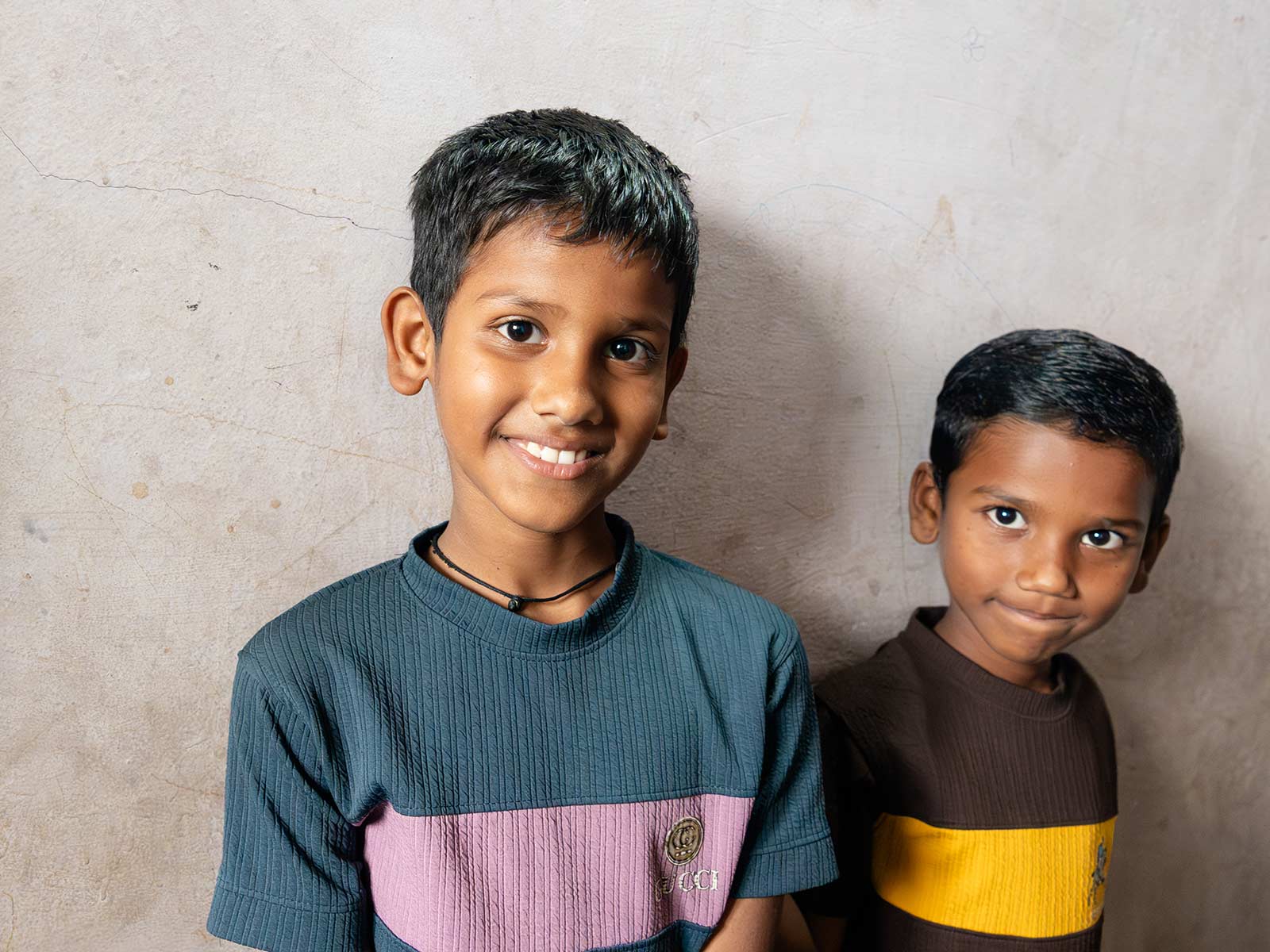 two little boys — brothers of a sponsored girl — smile in their home