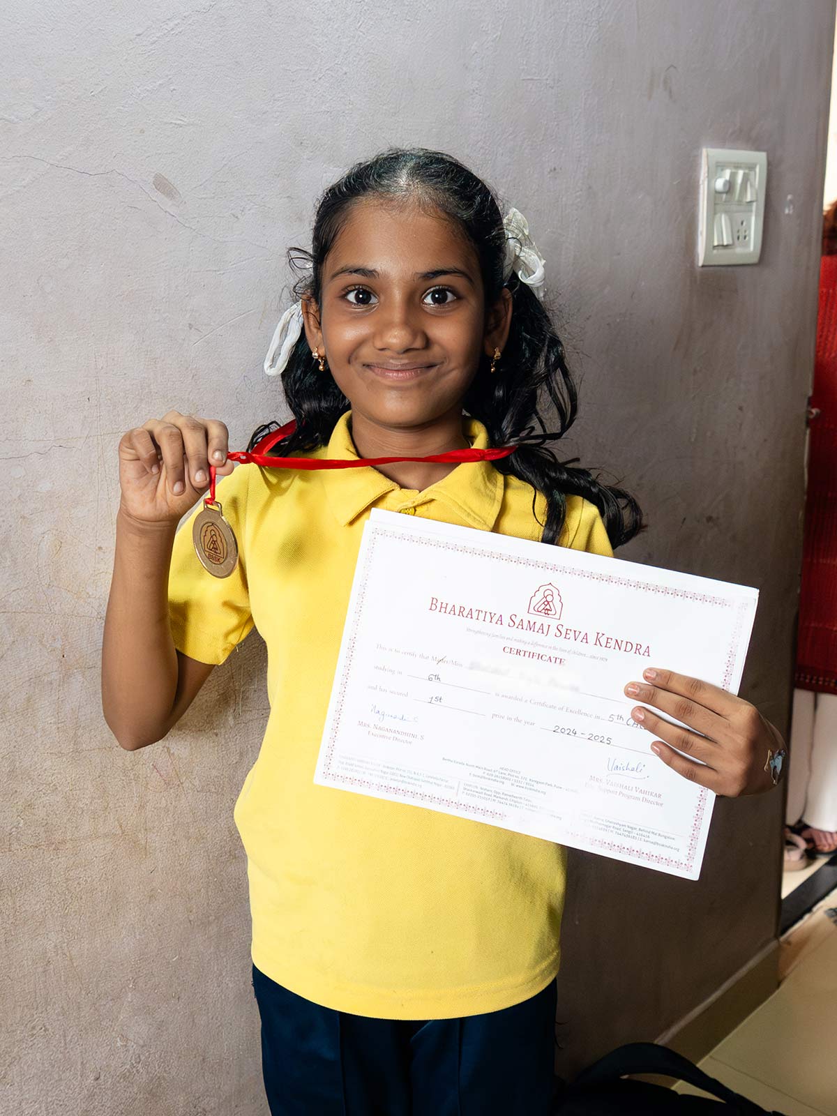 a proud sponsored girl in India holds up a certificate and medal she earned from reading