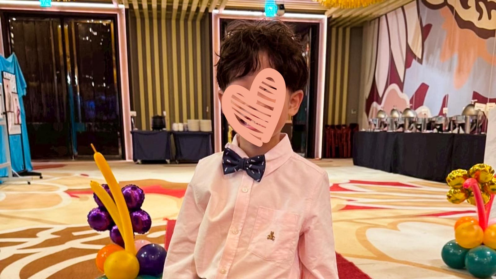a waiting child stands in a bowtie with a heart over his face, waiting to be adopted