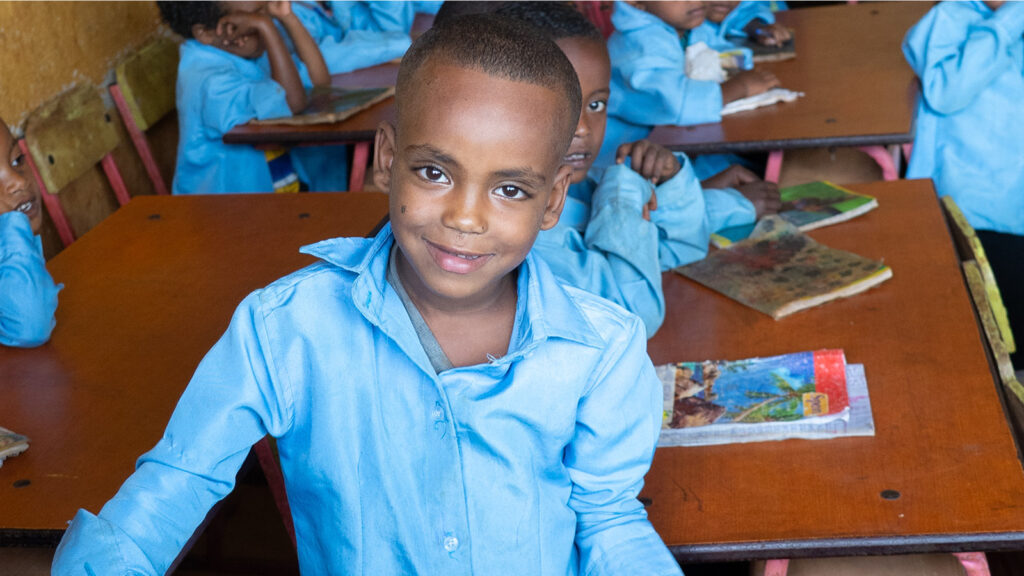Young boy standing in front of his desk at school in Ethiopia